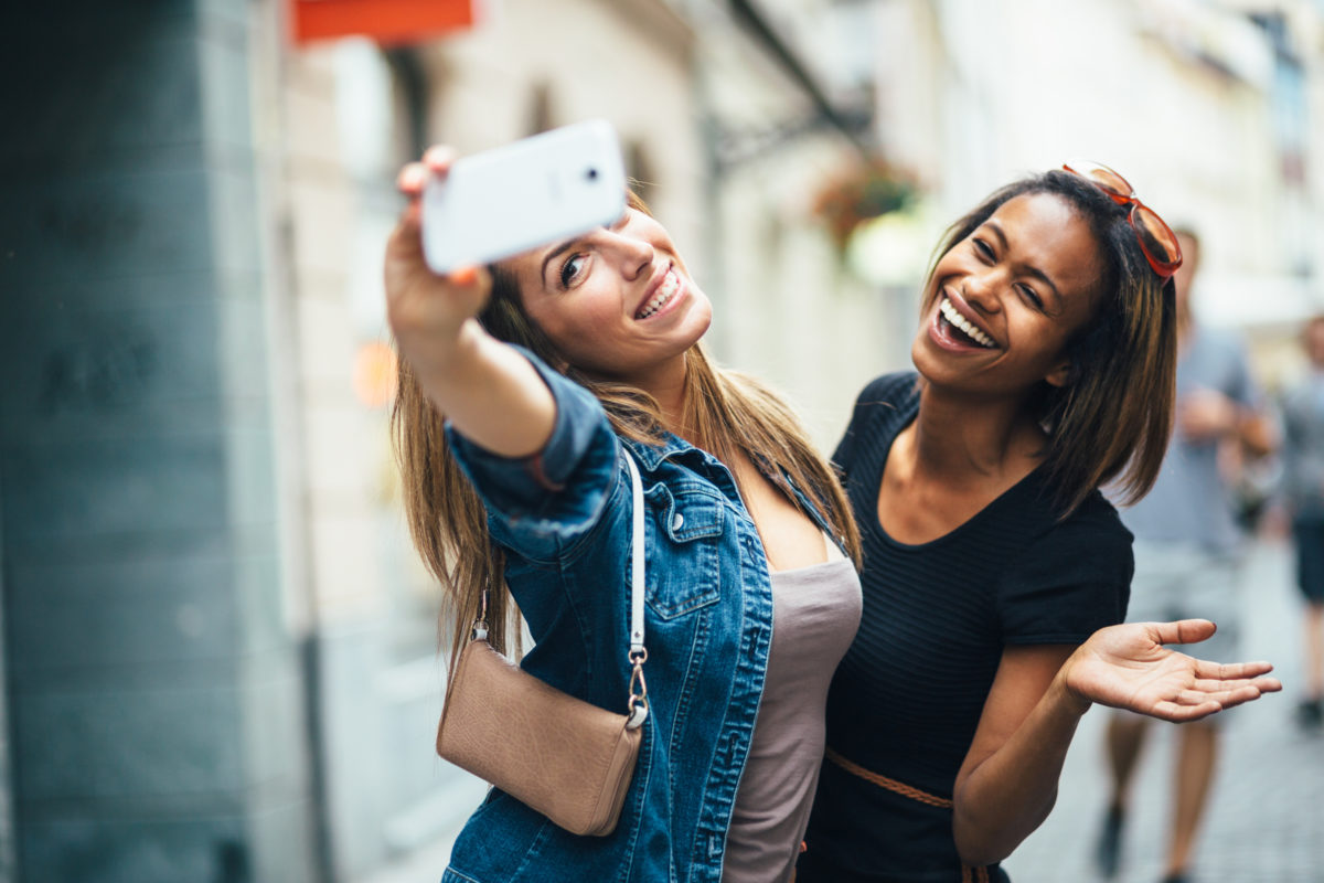 Two women laughing and taking a selfie outdoors