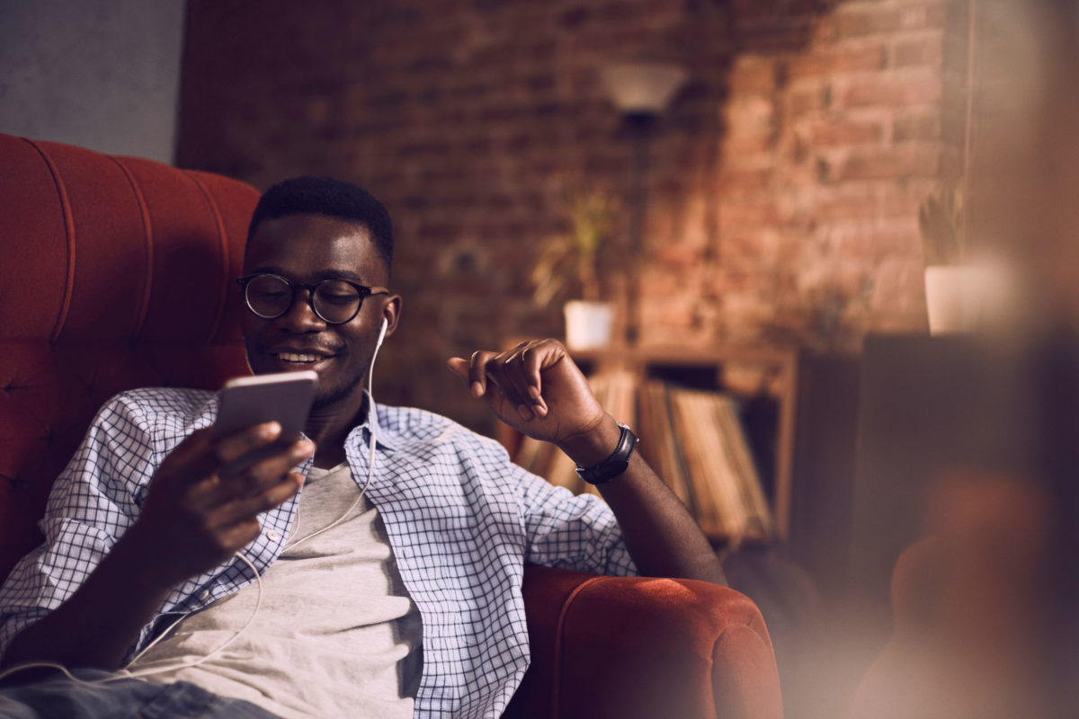 Young man on couch looking at phone with headphones