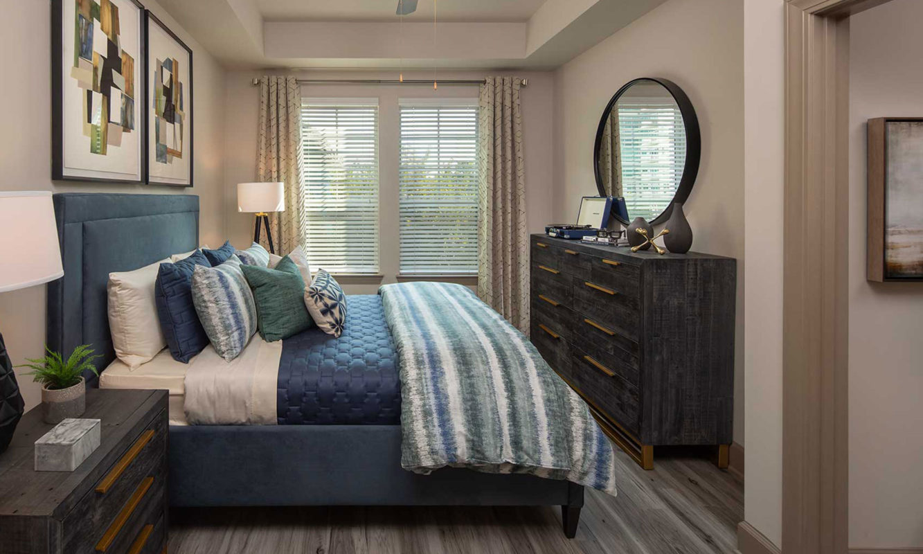 Bedroom with queen sized bed, dresser and nightstand, wood like floor, ceiling fan and large windows