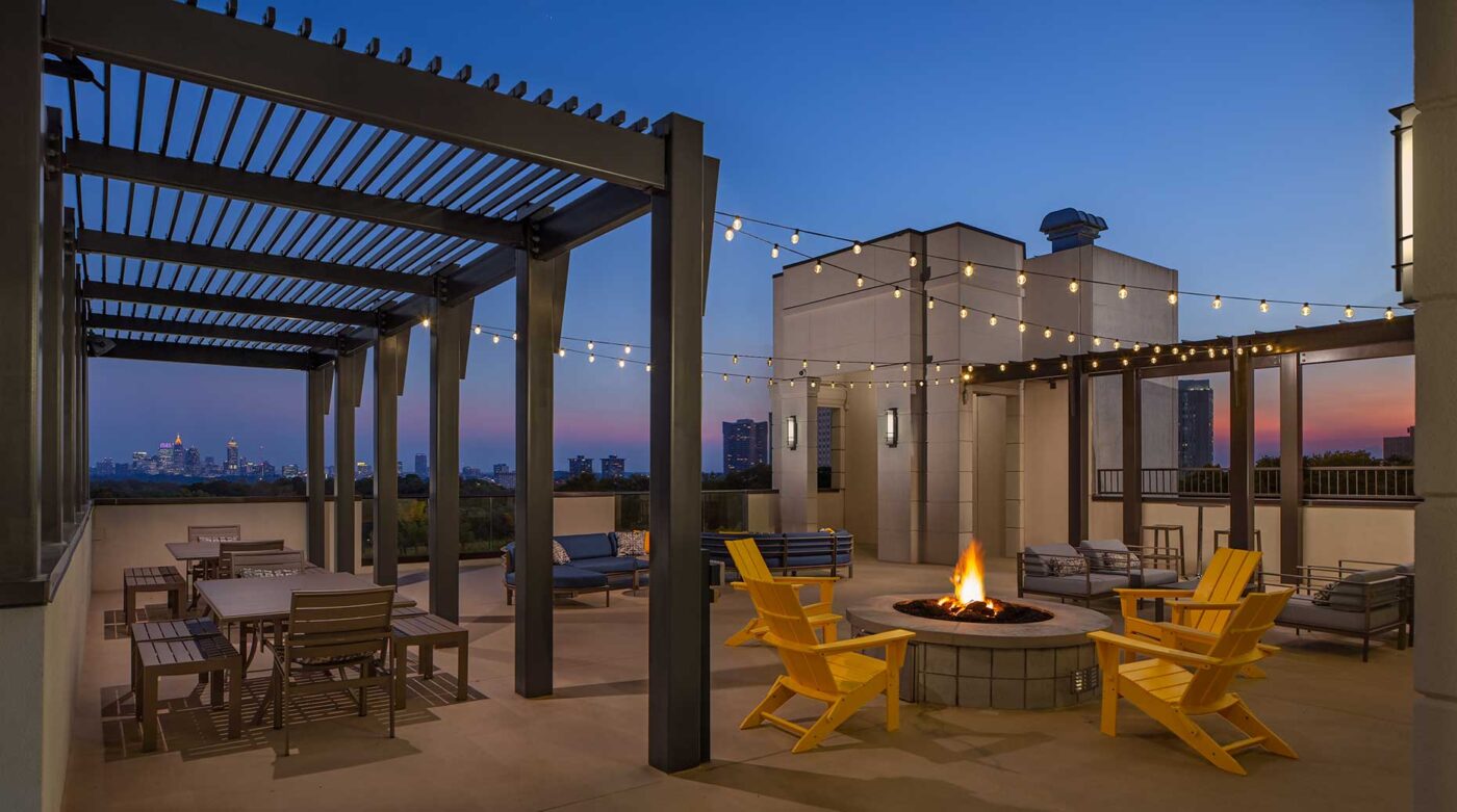 Dusk shot of rooftop fire pit with string lighting and tables and chairs